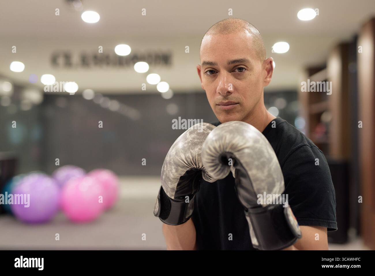 Uomo calvo ispanico che indossa guanti da pugilato che si posa come combattente o allenatore all'interno di una moderna palestra. Allenamento di combattimento, allenamento di boxe, coaching personale, AN Foto Stock