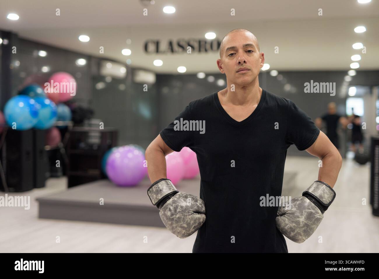 Uomo calvo ispanico che indossa guanti da pugilato che si posa come combattente o allenatore all'interno di una moderna palestra. Allenamento di combattimento, allenamento di boxe, coaching personale, AN Foto Stock