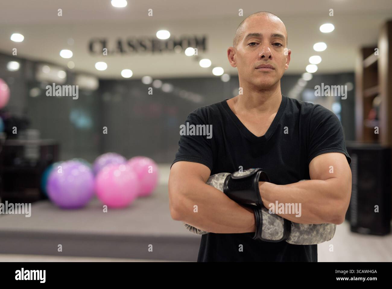 Uomo calvo ispanico che indossa guanti da pugilato che si posa come combattente o allenatore all'interno di una moderna palestra. Allenamento di combattimento, allenamento di boxe, coaching personale, AN Foto Stock