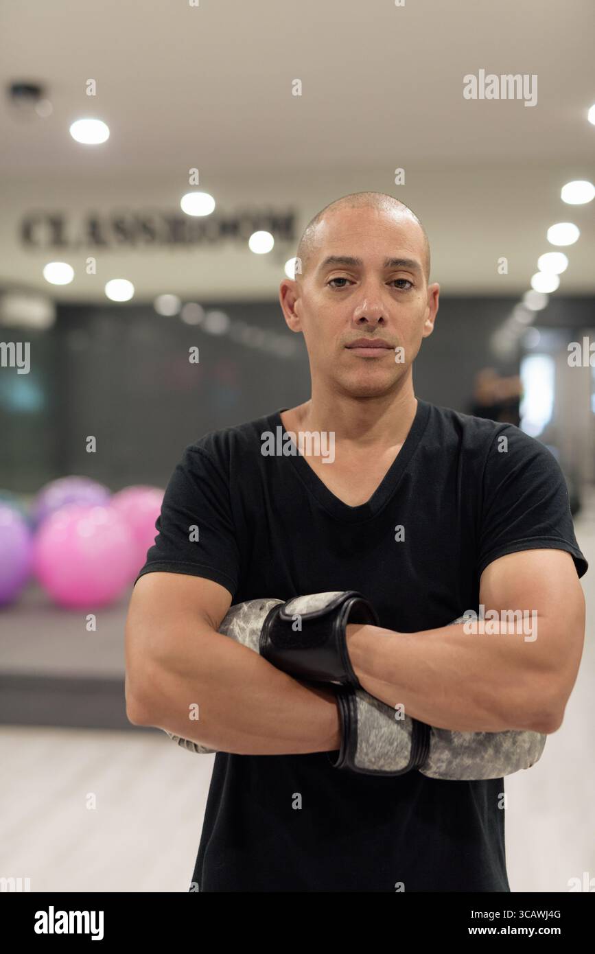 Uomo calvo ispanico che indossa guanti da pugilato che si posa come combattente o allenatore all'interno di una moderna palestra. Allenamento di combattimento, allenamento di boxe, coaching personale, AN Foto Stock
