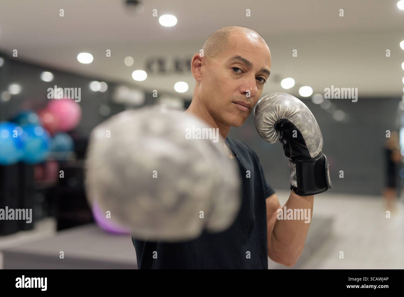 Uomo calvo ispanico che indossa guanti da pugilato che si posa come combattente o allenatore all'interno di una moderna palestra. Allenamento di combattimento, allenamento di boxe, coaching personale, AN Foto Stock
