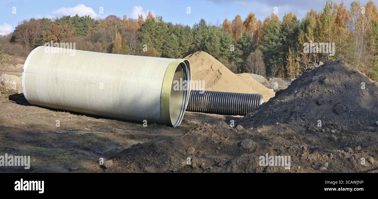 Grandi tubi fognari e un mucchio di sabbia in un cantiere forestale autunnale. Collage panoramico da diversi scatti all'aperto assolati del giorno di ottobre Foto Stock