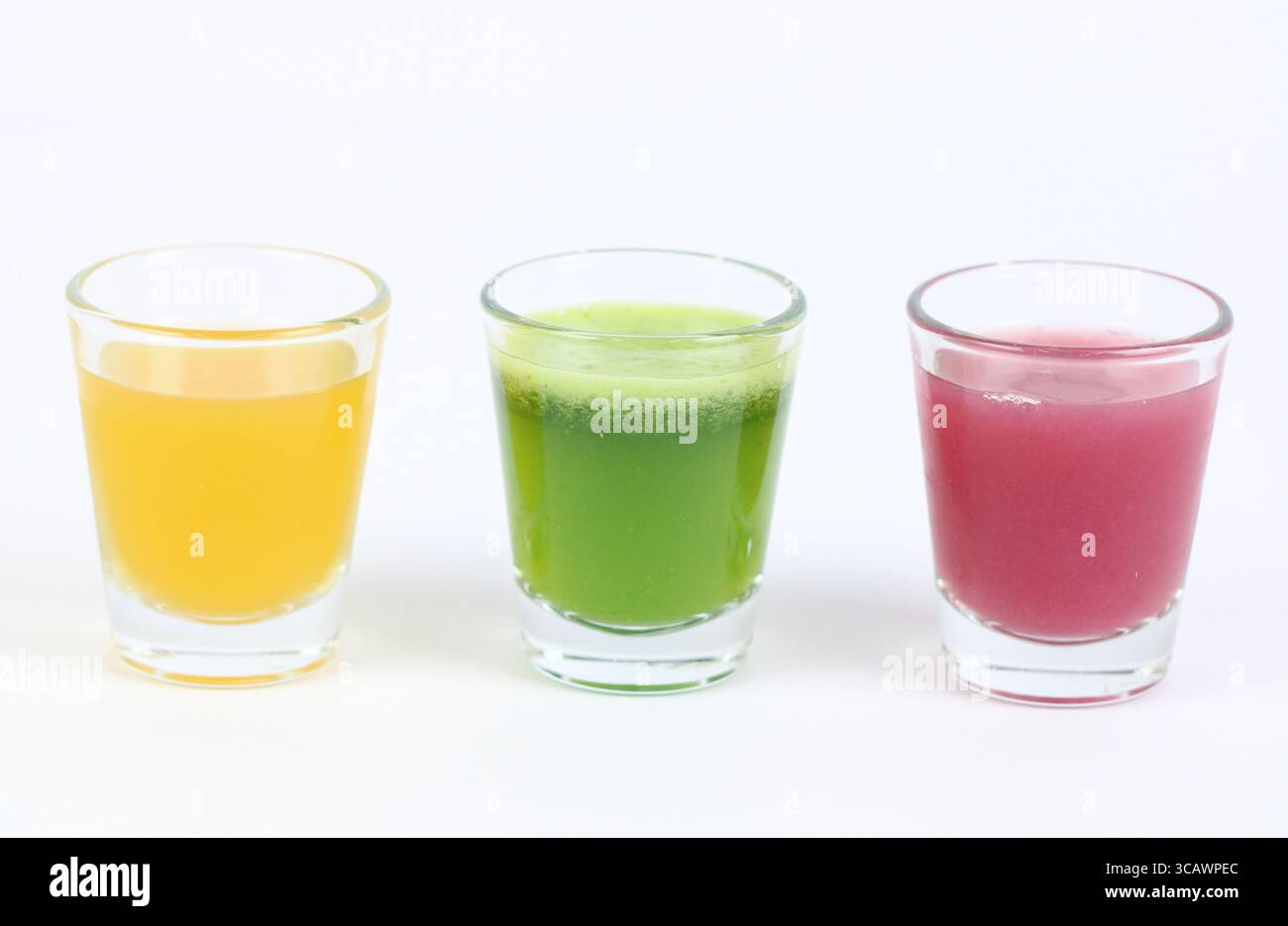 Tre shot di succo benessere colorati disposti in fila. Rappresenta la varietà nella nutrizione superalimentare, nella salute a base vegetale e nelle routine olistiche di benessere. Foto Stock