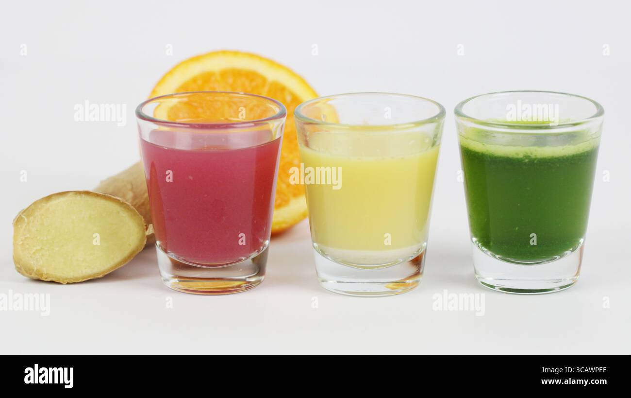 Trio di spremute benessere colorate con zenzero fresco e fetta di arancia. Simboleggia rimedi naturali, supporto immunitario e stile di vita sano. Foto Stock