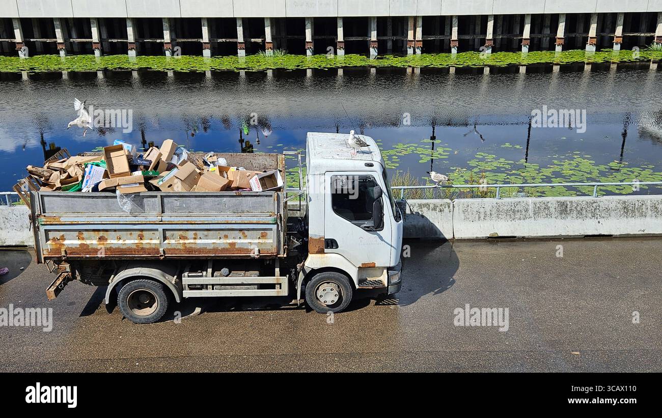Furgone per rifiuti rugginito di Canal con gabbiani e rifiuti di cartone. Gestione dei rifiuti urbani e concetto di riciclaggio. - Immagine stock catturata con smartphone