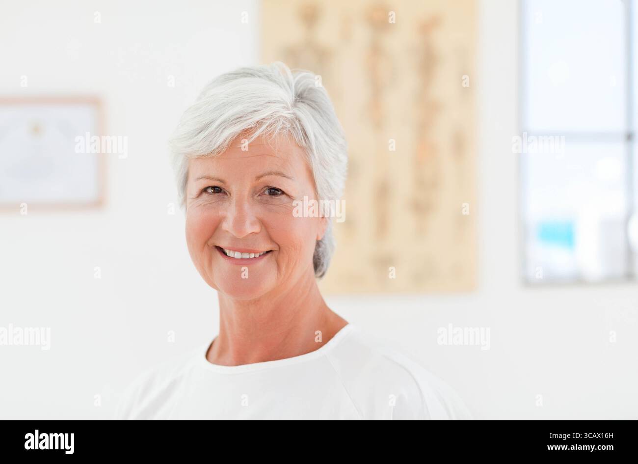 Donna bianca anziana sorridente mentre è seduta in clinica con cartella anatomica e certificato Foto Stock