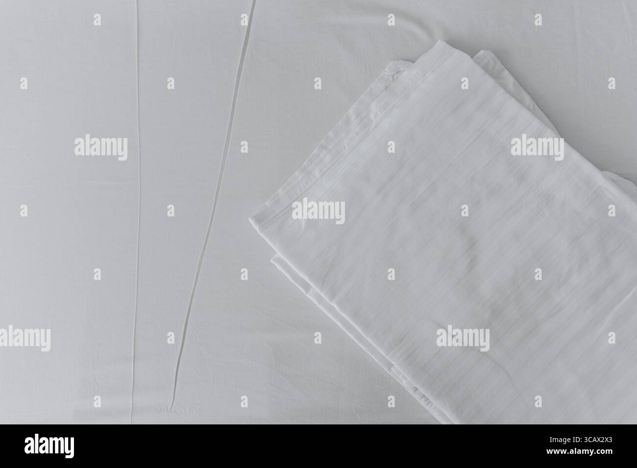 Biancheria da letto bianca ripiegata su un letto minimalista e pulito con texture morbide e motivo a strisce. Foto Stock