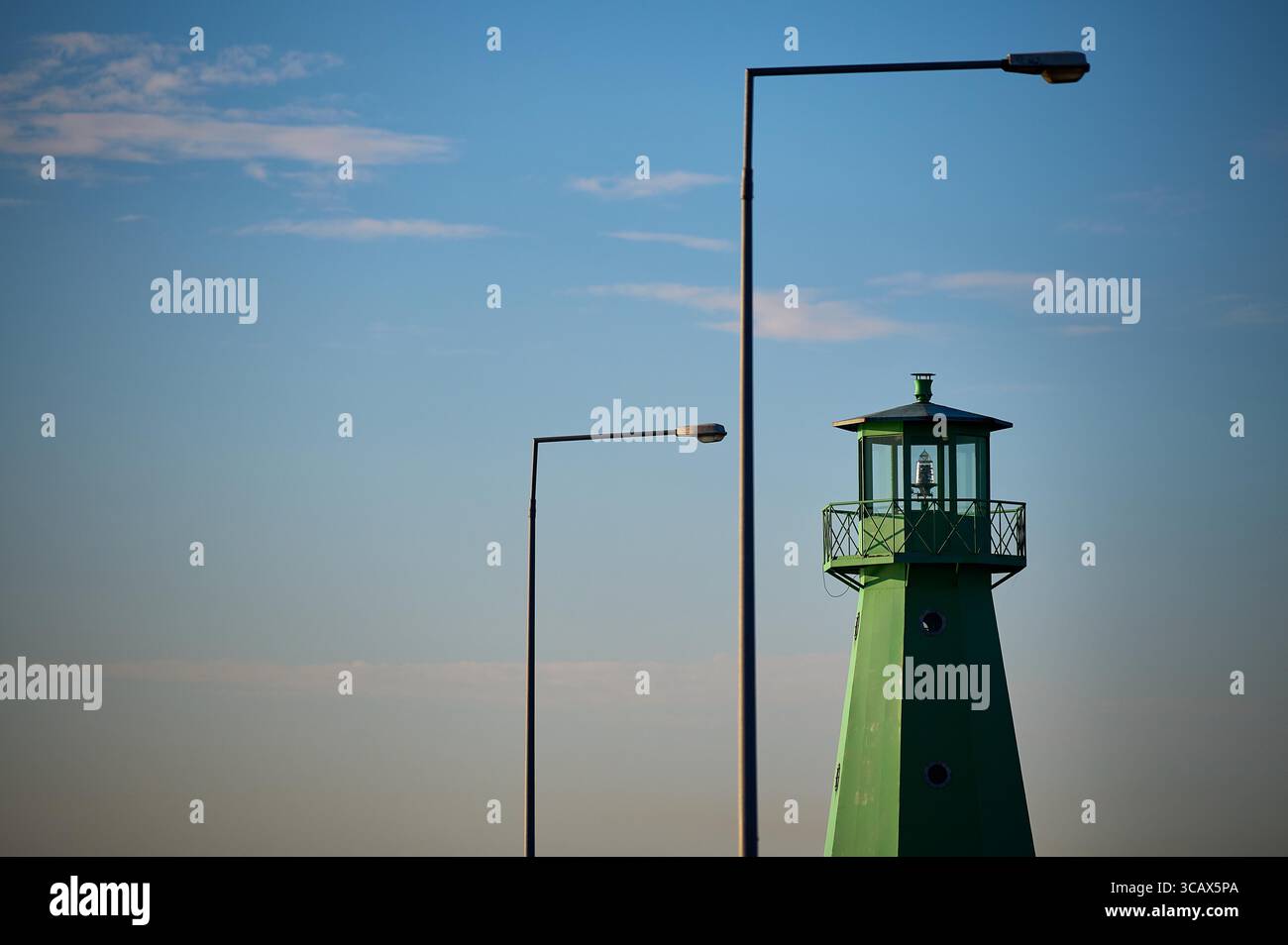 Ambiente minimalista con faro verde e doppi lampioni sul cielo limpido. Foto Stock