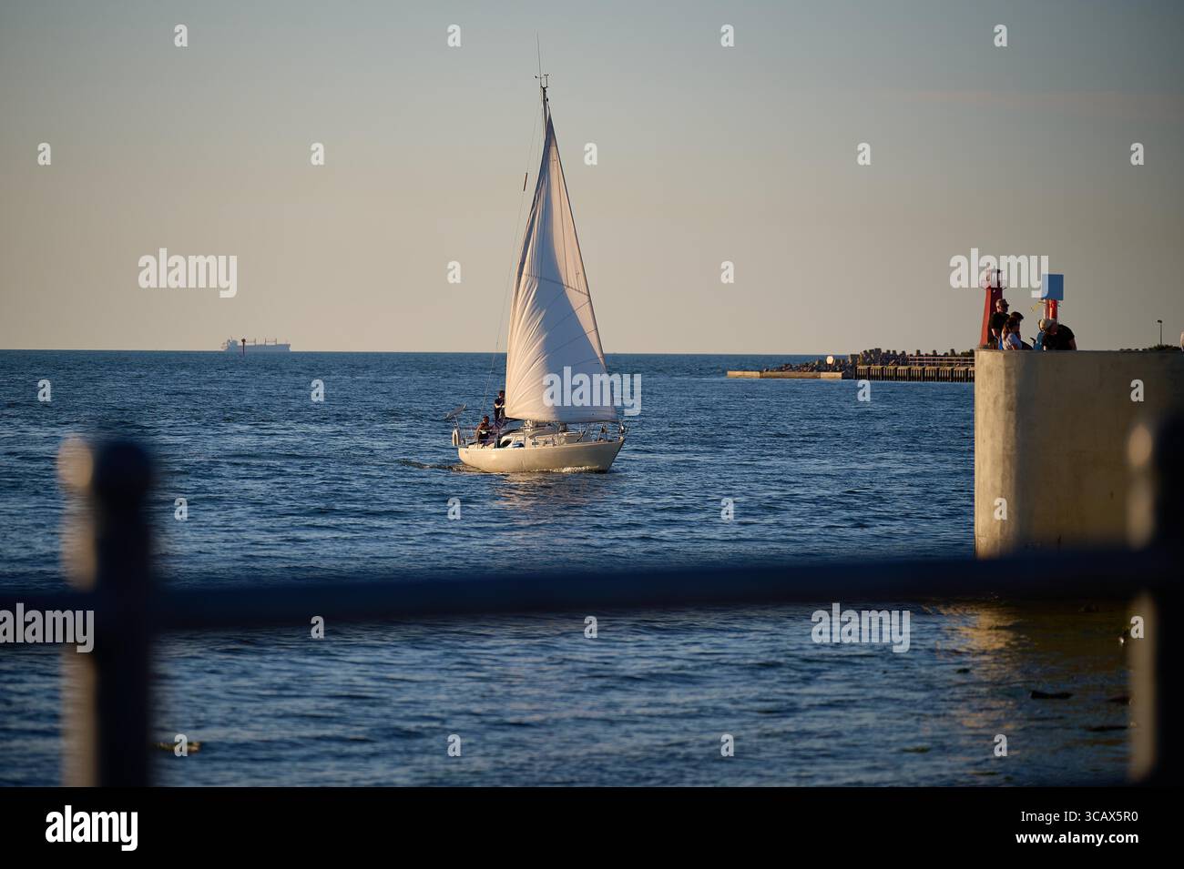 Barca a vela bianca illuminata dalla luce dorata del sole che entra nel Mar Baltico aperto dal porto di Danzica. Foto Stock