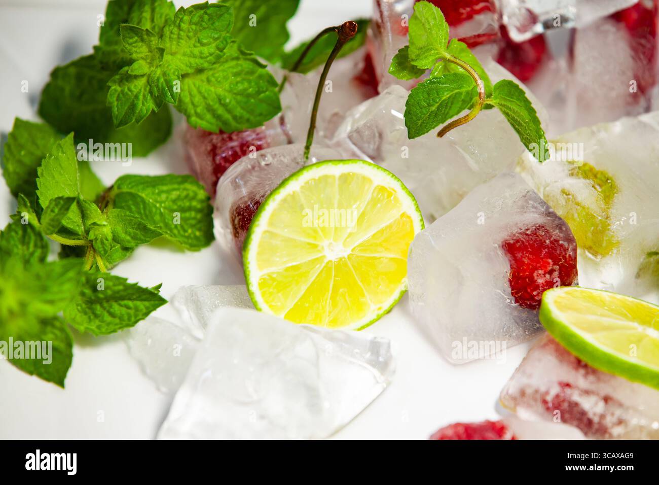Lime rinfrescante, menta e lamponi su cubetti di ghiaccio scioglienti. Il sapore estivo naturale in un ambiente vivace e piatto. Foto Stock