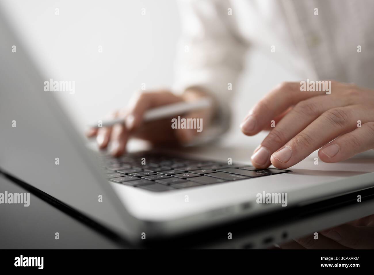 Moderno uomo d'affari che utilizza un computer portatile in un'elegante area di lavoro. Ambiente alla moda con tavolo in legno e accessori tecnologici. Concentrati sulle mani e sull'ambiente di lavoro elegante Foto Stock