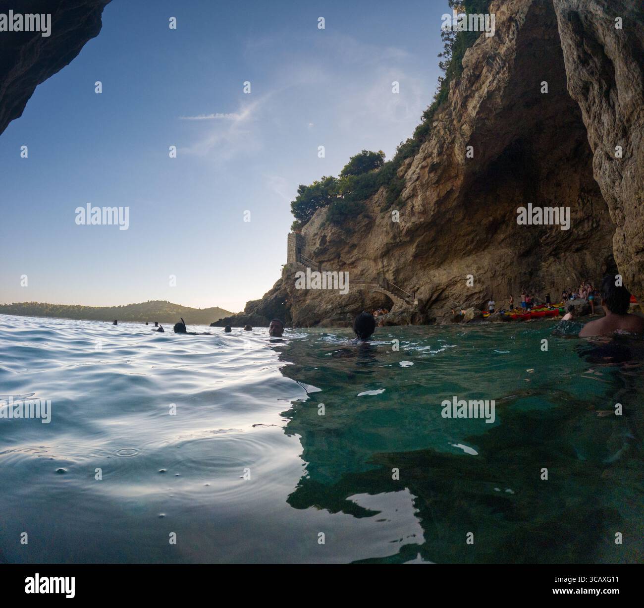 Dubrovnik, Croazia - 12 settembre 2023: I kayak si fermano in una grotta durante un tour al tramonto. Le persone nuotano e si rilassano prima di continuare il tour. Foto Stock