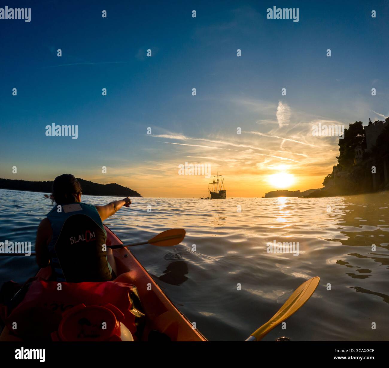 Dubrovnik, Croazia - 12 settembre 2023: Un kayaker punta verso una replica di galeone durante un tour al tramonto. I turisti apprezzano la vista. Foto Stock