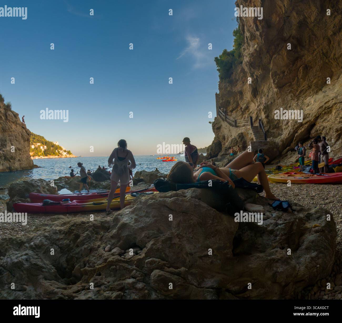 Dubrovnik, Croazia - 12 settembre 2023: I turisti si rilassano dopo un tour in kayak al tramonto, godendosi la spiaggia e il bellissimo paesaggio. Foto Stock