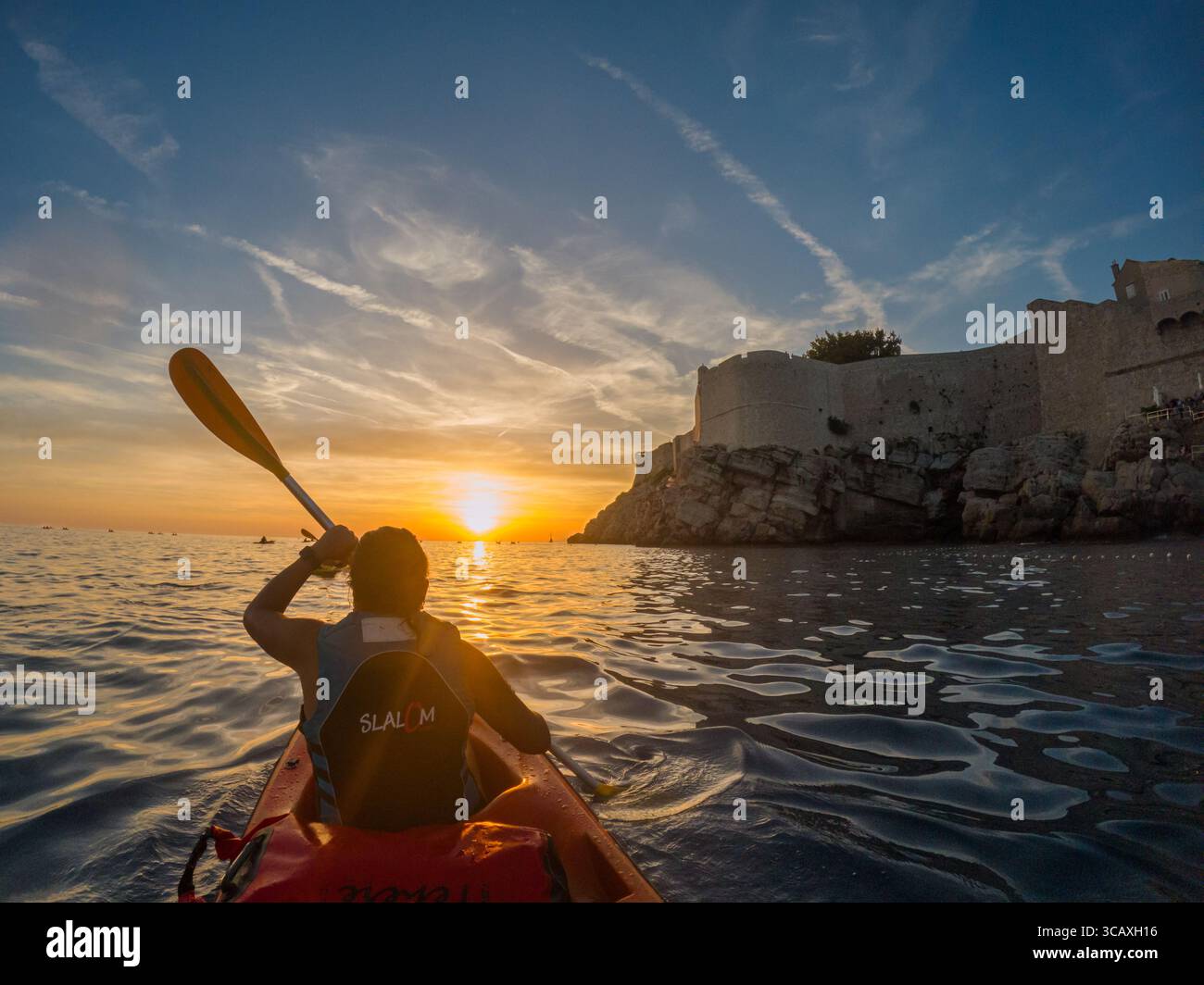 Dubrovnik, Croazia - 12 settembre 2023: Un kayak si dirige verso il tramonto durante un tour guidato lungo la costa vicino alle mura della città vecchia. Foto Stock