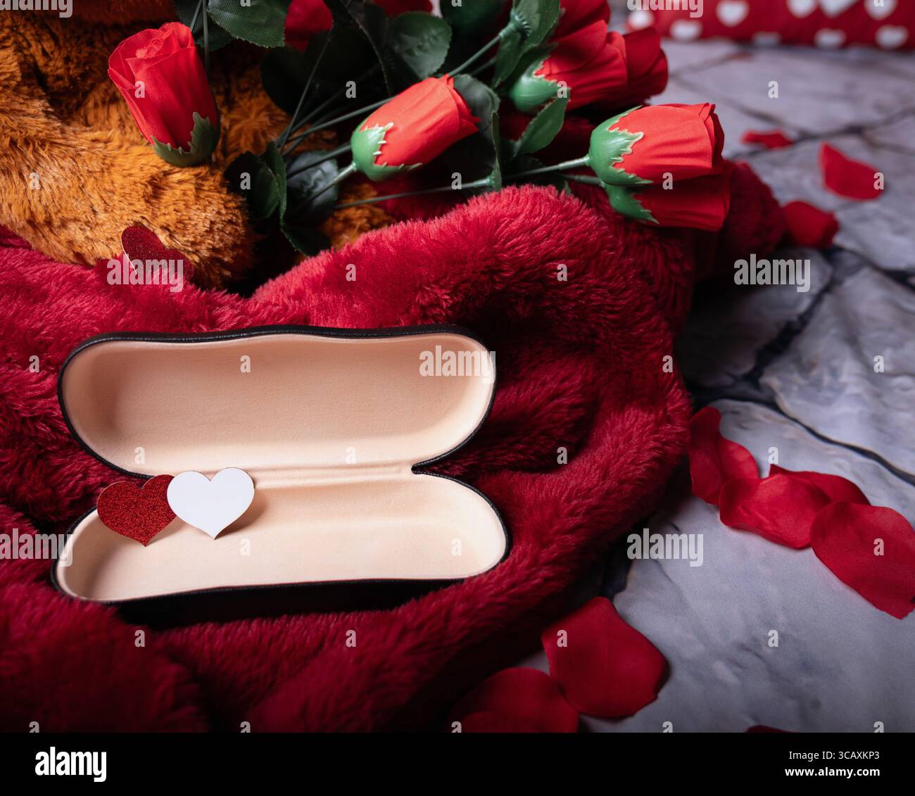 Primo piano di una custodia con obiettivo aperto contenente due piccole forme di cuore rosse e bianche, promozioni di San Valentino e concetto di visione Care. Foto Stock