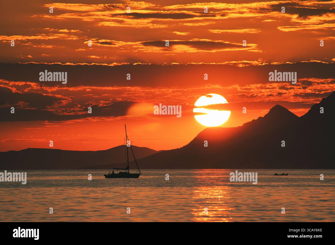 Tramonto dorato sul mare Adriatico con barca a vela e montagne dalle linee sagomate Foto Stock