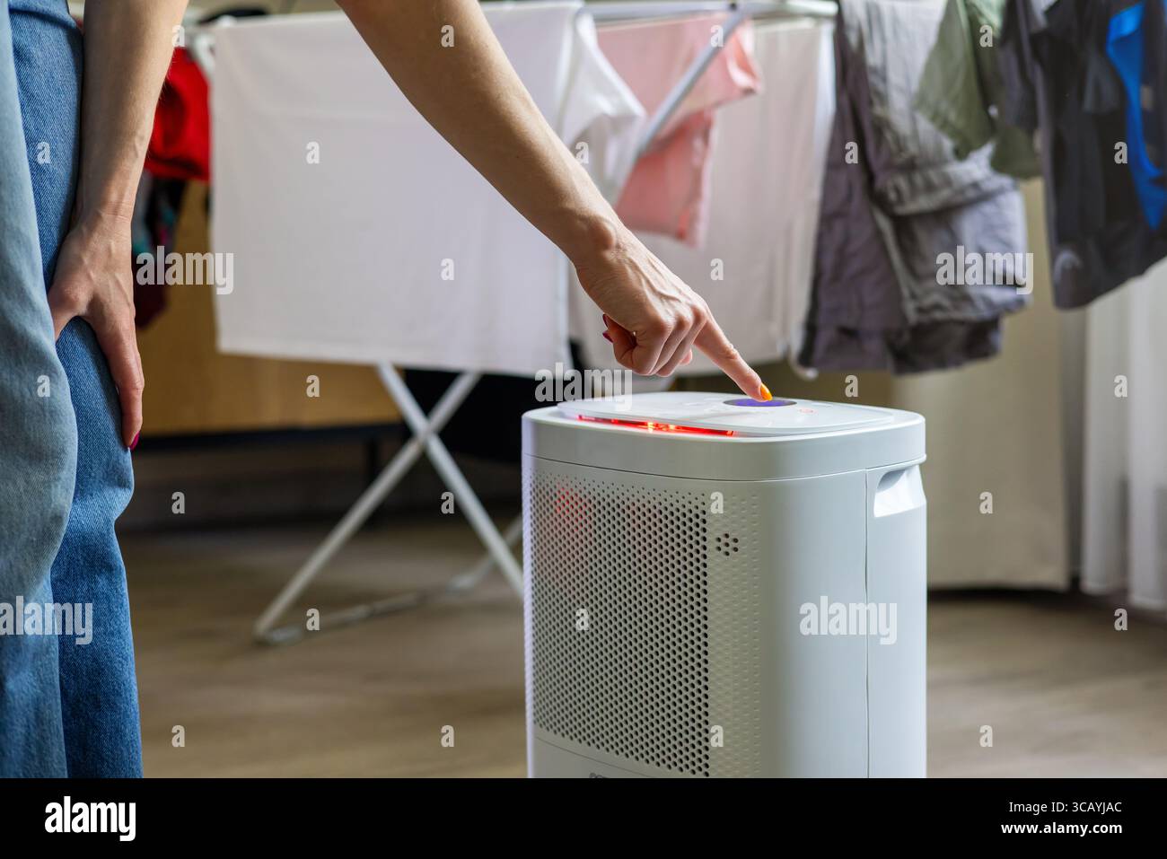 donna ha impostato il deumidificatore nella stanza di casa per raccogliere l'umidità dal bucato. controllo dell'umidità dell'aria dell'abitazione Foto Stock