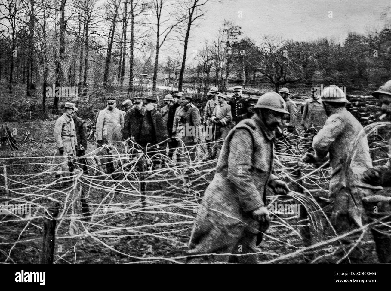 Il principe Alexandre di Serbia, il presidente francese, e il comandante in capo osservano i soldati francesi che installano filo spinato sulla terza linea durante la prima guerra mondiale. Questa rara immagine cattura i preparativi difensivi dietro le linee del fronte, con alti funzionari che supervisionano le operazioni. Ambientato in una foresta invernale, riflette la diplomazia in tempo di guerra e il coordinamento militare tra Serbia e Francia sul fronte occidentale. Foto Stock