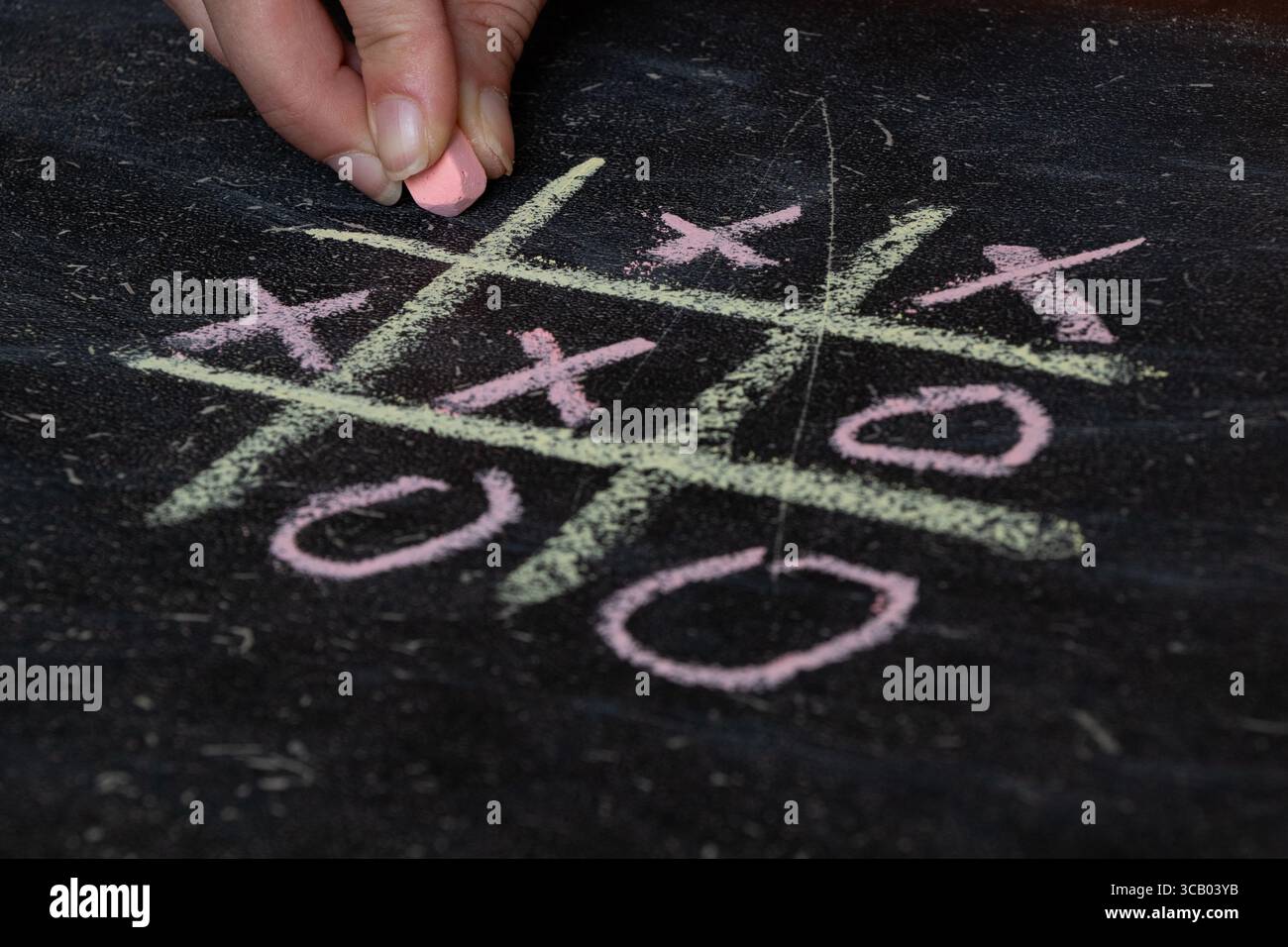 Donna che disegna a mano il dito tac sul tabellone nero della scuola con gesso, gioca a giochi da tavolo Foto Stock