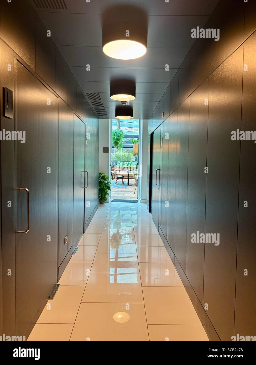 Corridoio elegante e moderno con pavimenti bianchi lucidi e luce calda che conduce ad una luminosa terrazza esterna al Furnas Octant Hotel. Foto Stock