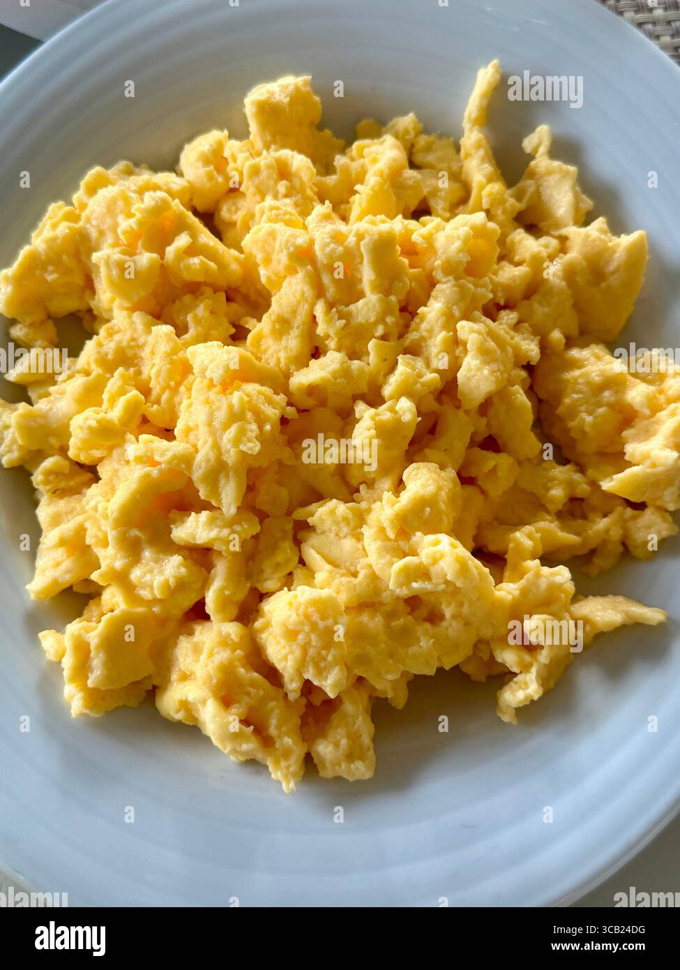 Primo piano di soffici uova strapazzate servite su un piatto bianco, con un piatto classico per la colazione. Foto Stock