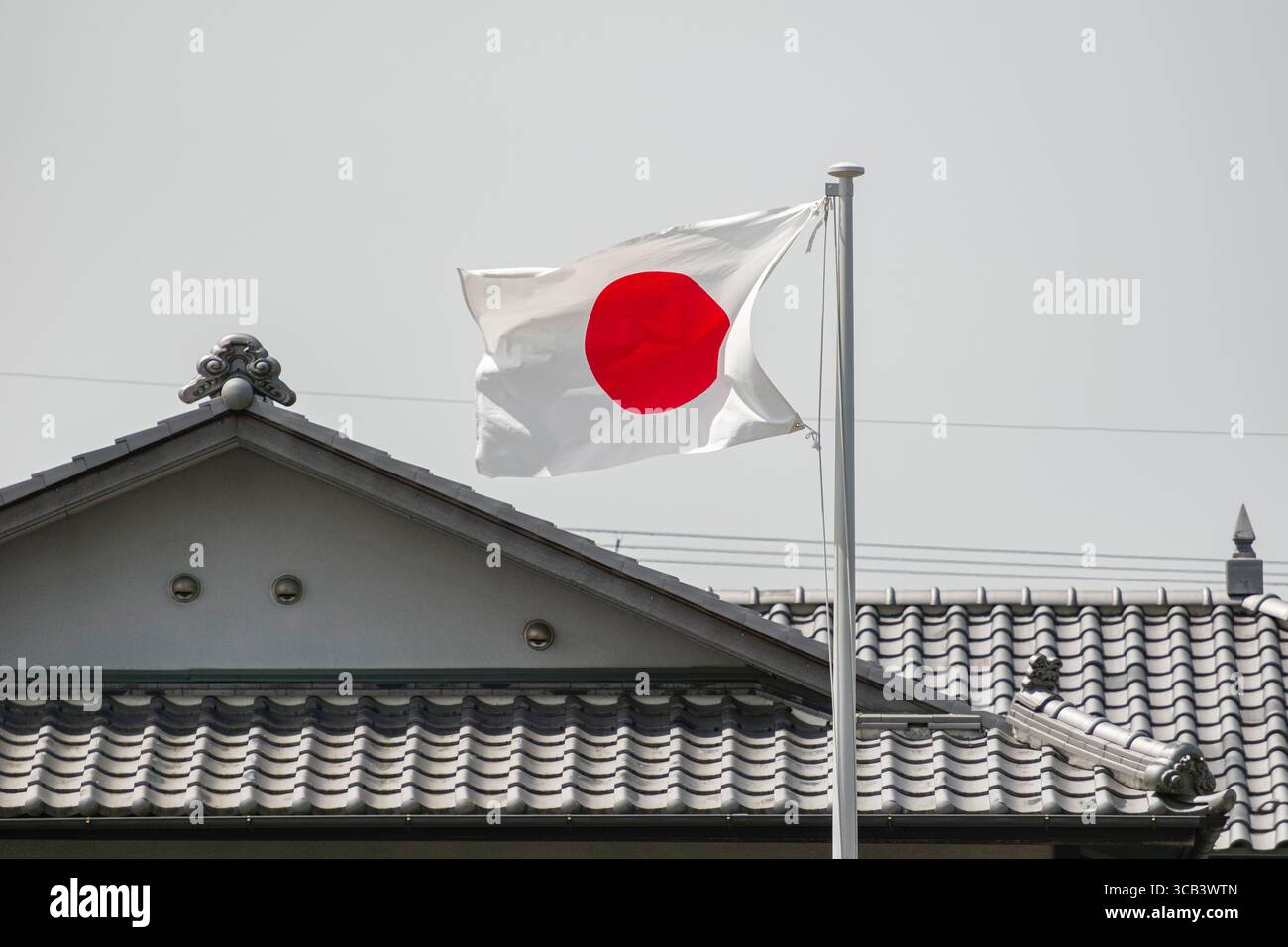 La bandiera nazionale del Giappone ondeggia orgogliosamente sopra un tradizionale tetto giapponese, simboleggiando il patrimonio culturale e l'orgoglio nazionale. Kyoto, Giappone Foto Stock