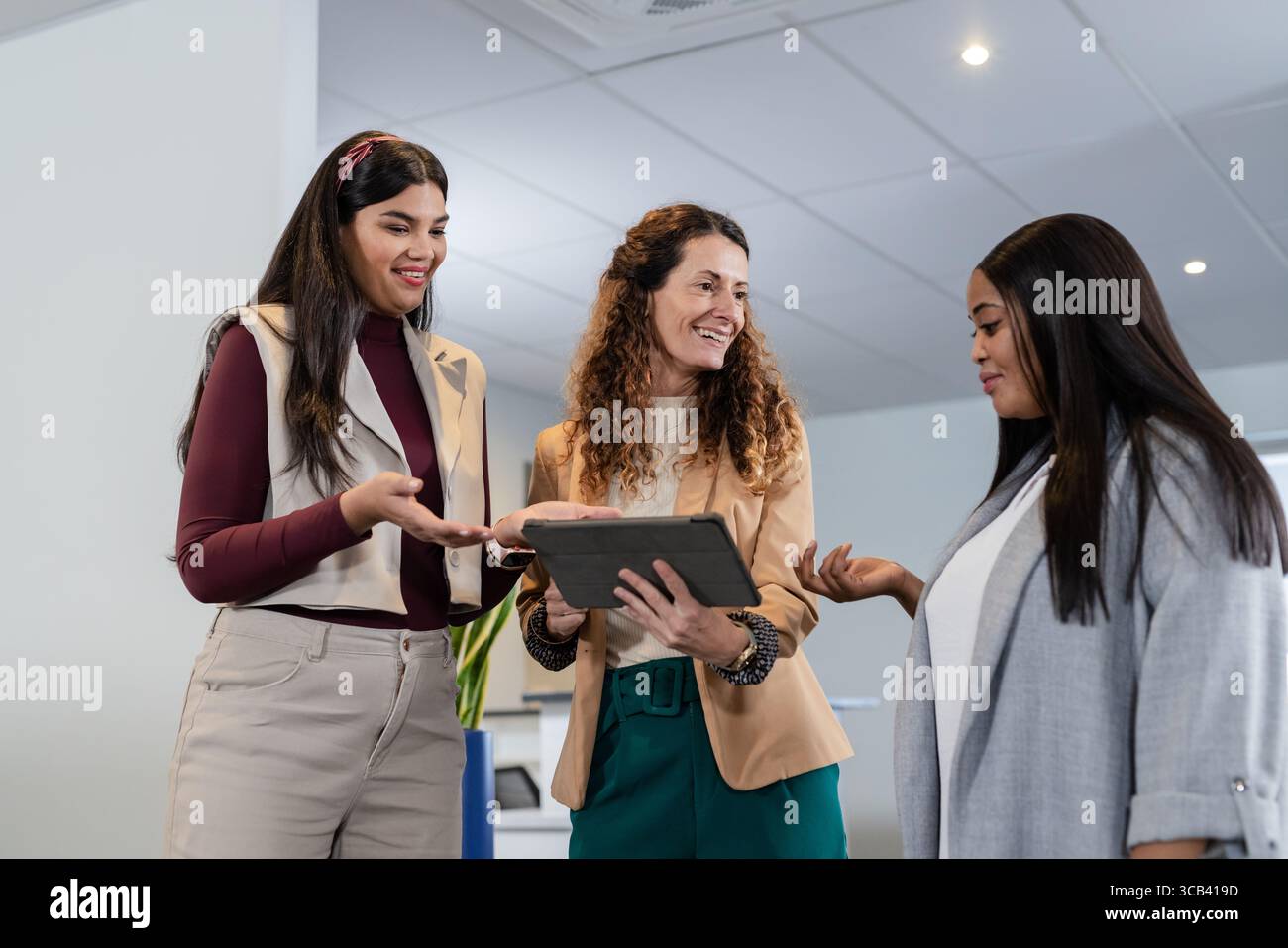 Diverse donne colleghi che indossano blazer che collaborano con tablet digitali in ufficio e in stabilimento Foto Stock