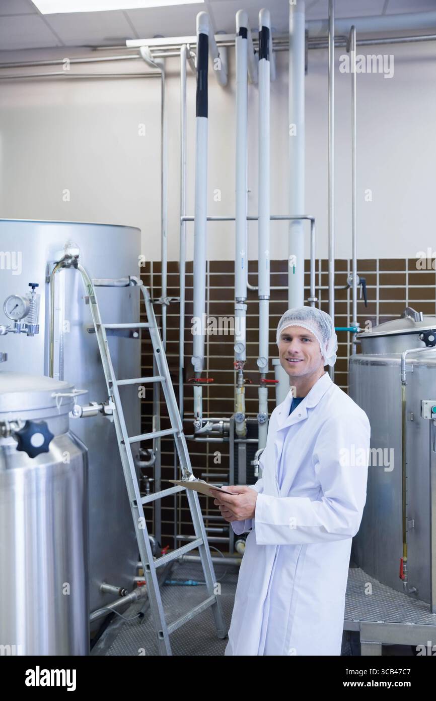 Tecnico che ispeziona i serbatoi e le tubazioni in metallo con valvole e manometri nella sala dell'impianto di produzione di bevande Foto Stock