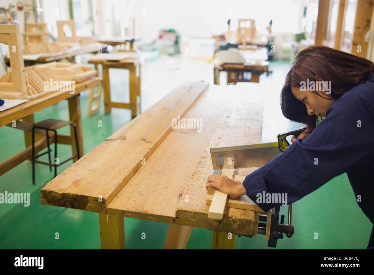 Lavoratrice del legno asiatica che guida la tavola attraverso il tavolo ha visto in giacca da lavoro della marina presso l'officina di falegnameria Foto Stock