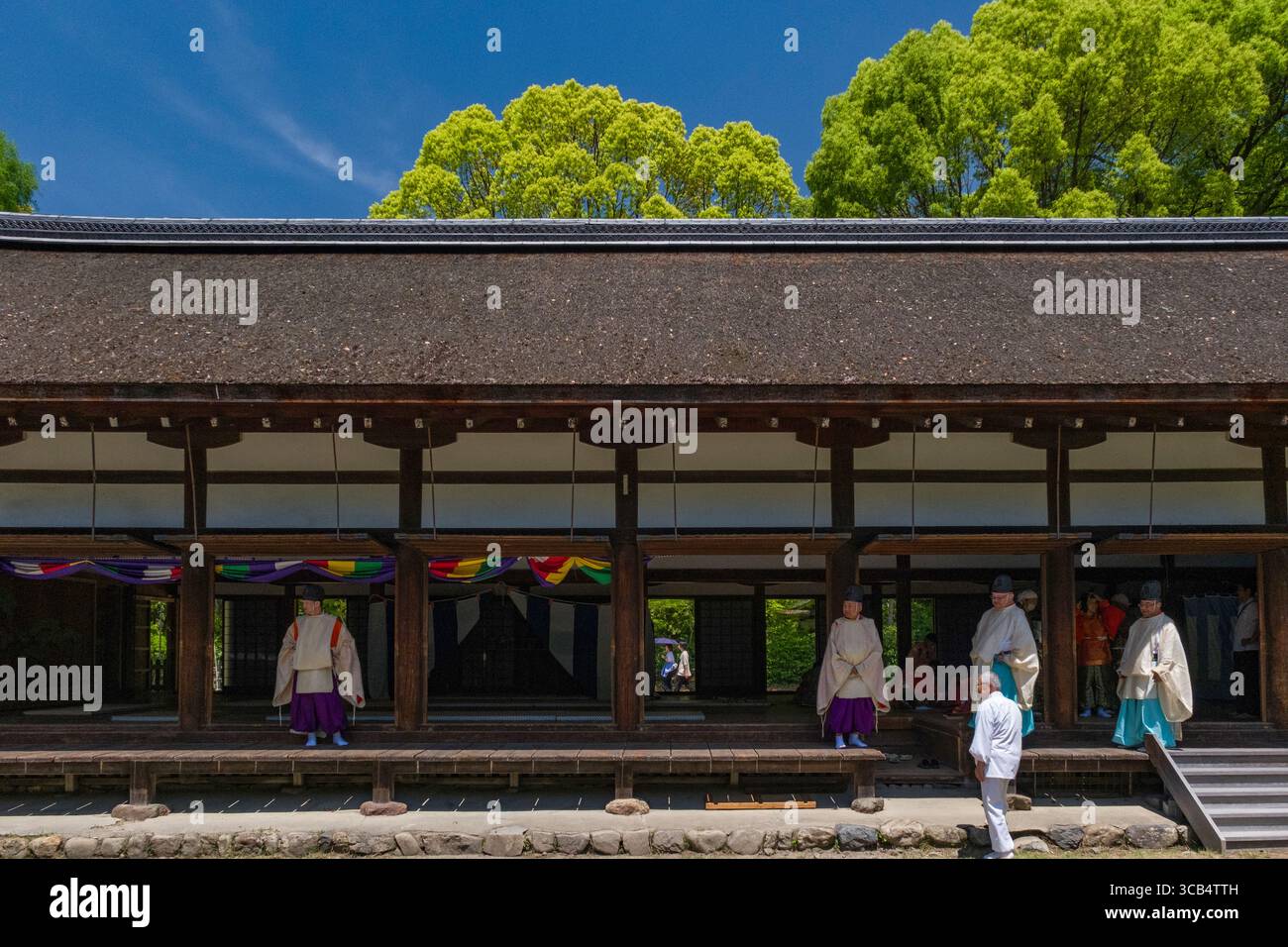 L'antico tempio giapponese con architettura tradizionale ospita un evento cerimoniale. I partecipanti all'abbigliamento tradizionale si trovano sotto il cielo azzurro. Foto Stock