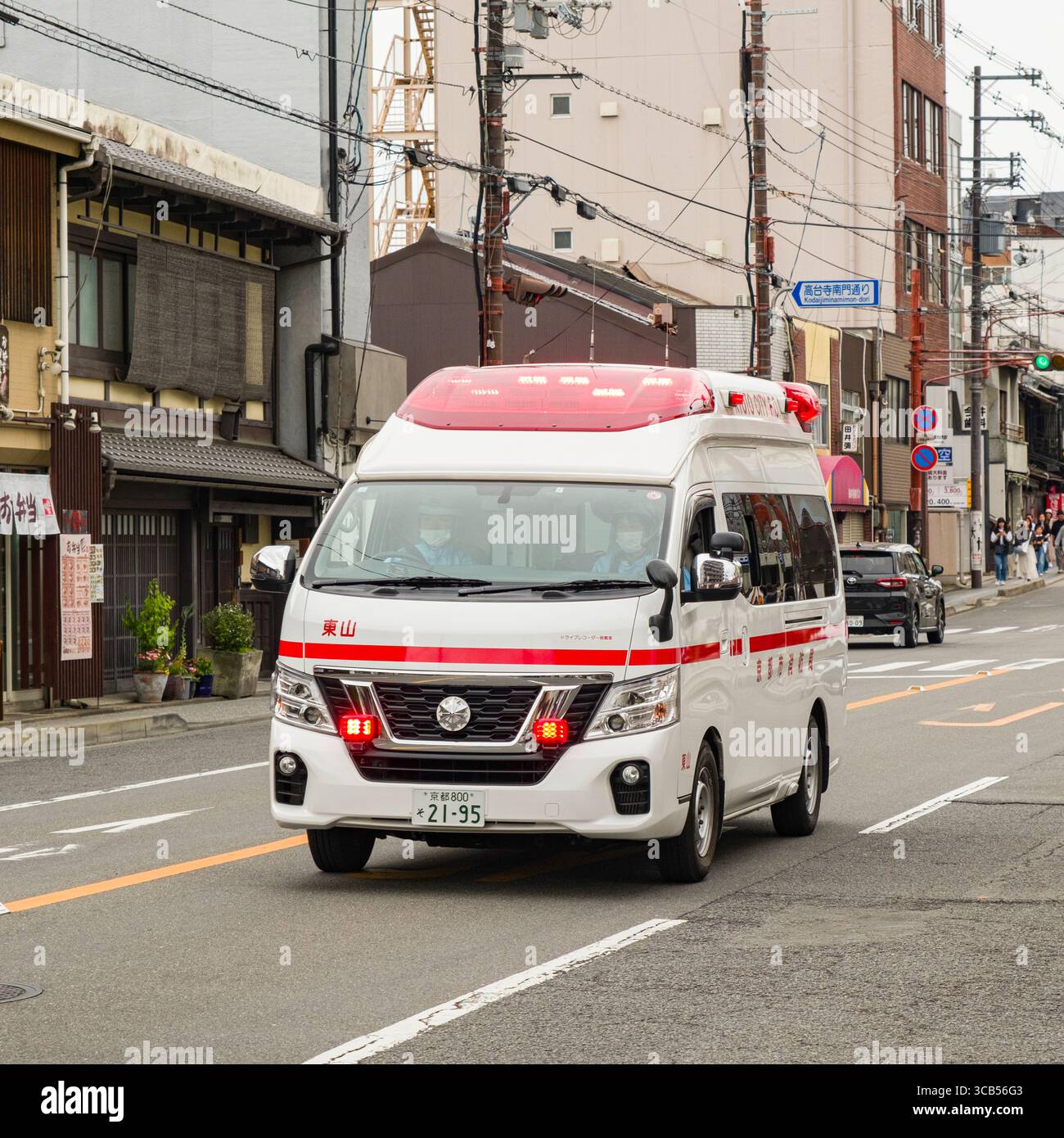 Un'ambulanza bianca con contrassegni rossi accelera attraverso una strada urbana trafficata, rispondendo a una chiamata di emergenza. Rappresenta una rapida assistenza medica, Kyoto Foto Stock