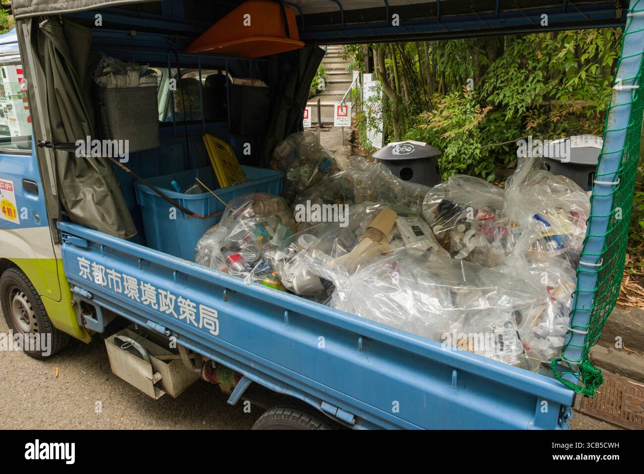 Camion per la gestione dei rifiuti riempito con sacchetti di plastica contenenti materiali di scarto, parcheggiato vicino a un'area verde in un ambiente urbano, Ukyo Ward, Kyoto, Giappone Foto Stock