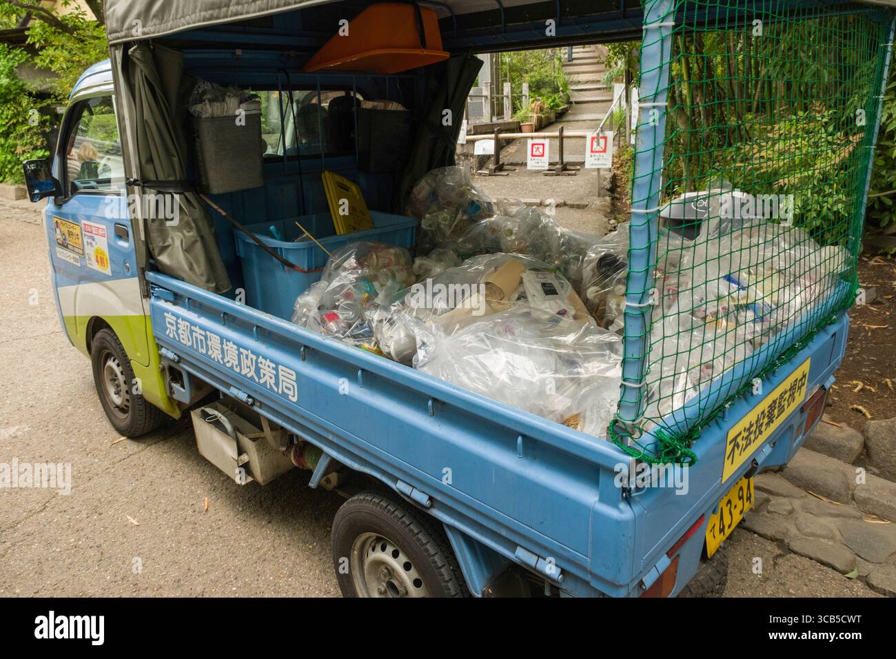 Camion per la gestione dei rifiuti riempito con sacchetti di plastica contenenti materiali di scarto, parcheggiato vicino a un'area verde in un ambiente urbano, Ukyo Ward, Kyoto, Giappone Foto Stock