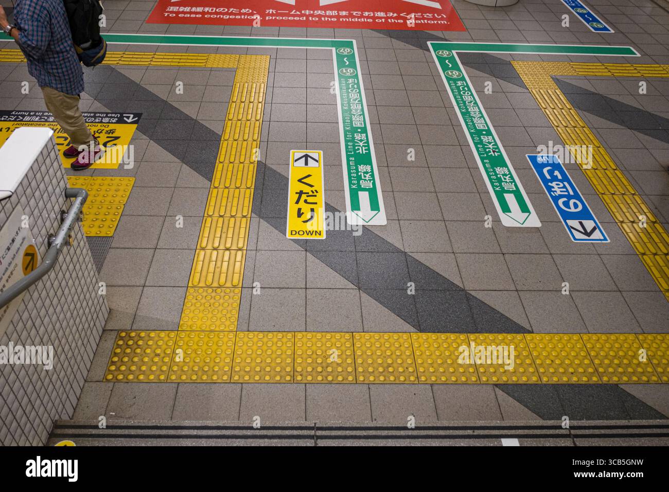 Un pendolare passa attraverso una stazione della metropolitana, navigando seguendo i segnali stradali direzionali. La pavimentazione tattile gialla vibrante aiuta gli ipovedenti, Kyoto Foto Stock