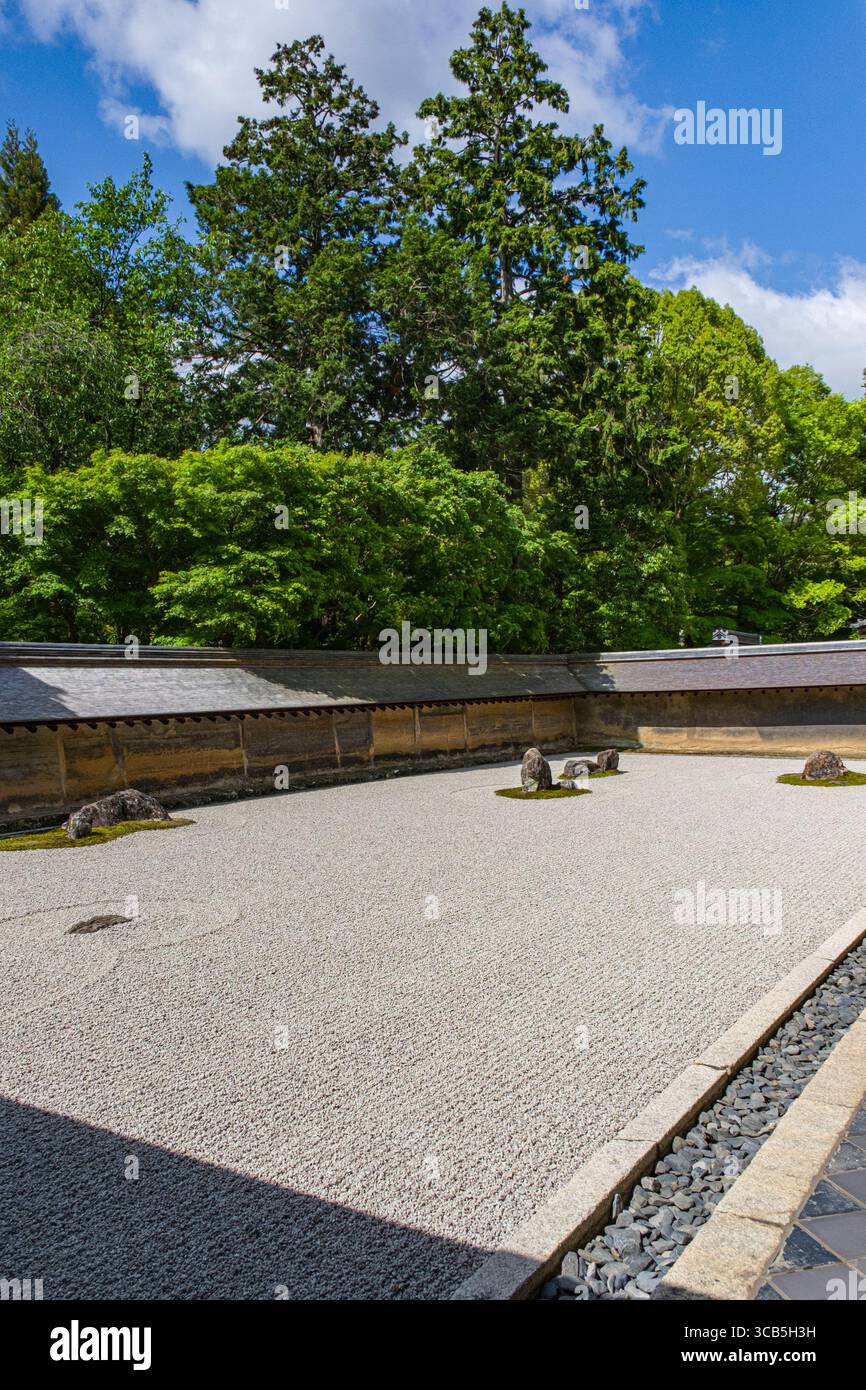 Kare-Sansui paesaggio secco giardino Zen a Ryōan-ji caratterizzato da rocce e ghiaia meticolosamente disposte. Circondato da lussureggianti alberi verdi, Kyoto, Giappone Foto Stock
