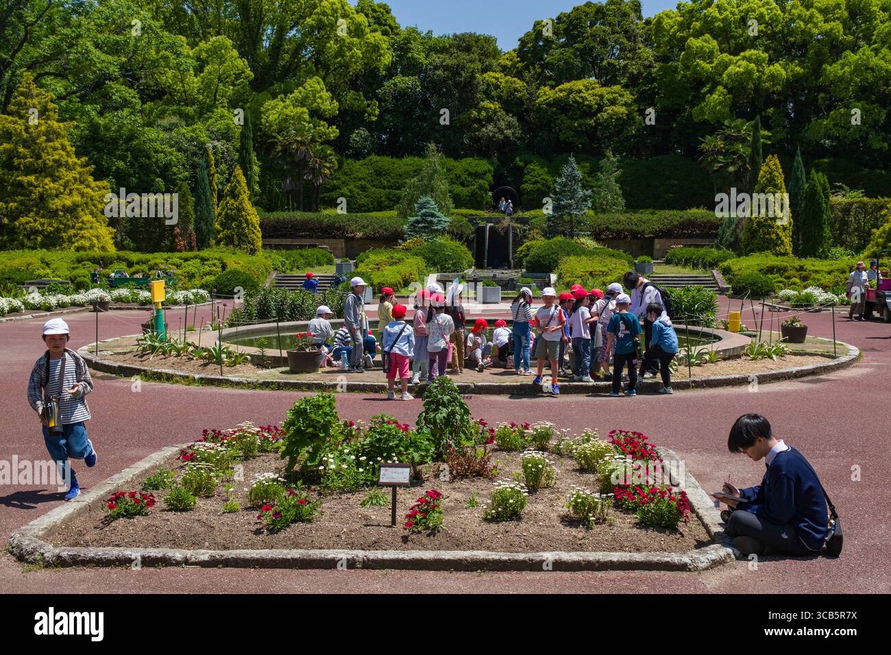 Un gruppo di bambini partecipa a un'attività scolastica all'aperto in un lussureggiante giardino botanico, circondato da una vegetazione vivace e fiori colorati Foto Stock