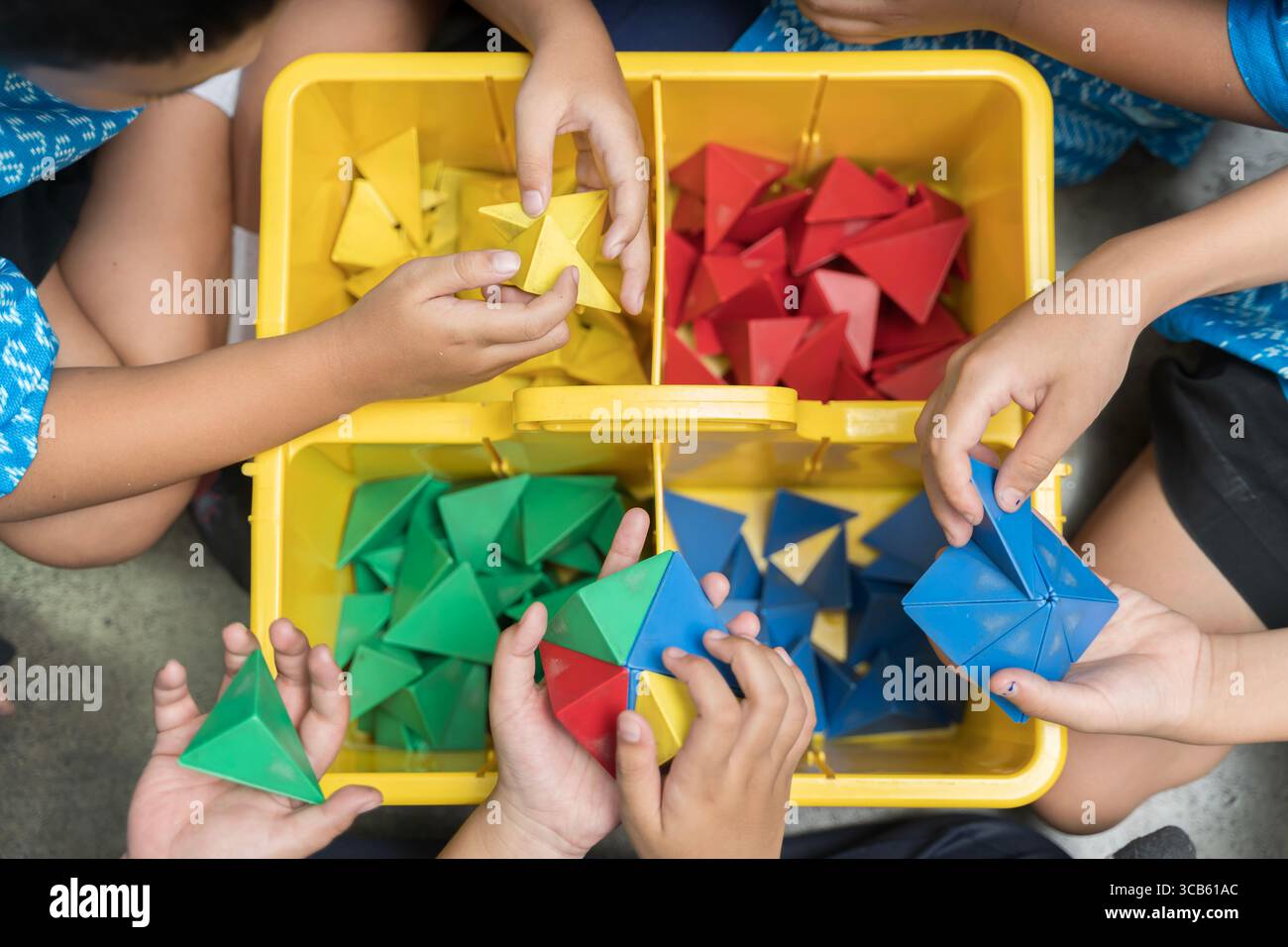 Vista dall'alto delle mani dei bambini che giocano con colorate forme geometriche in plastica 3D in una scatola gialla. Attività divertenti ed educative che promuovano la creatività, Foto Stock
