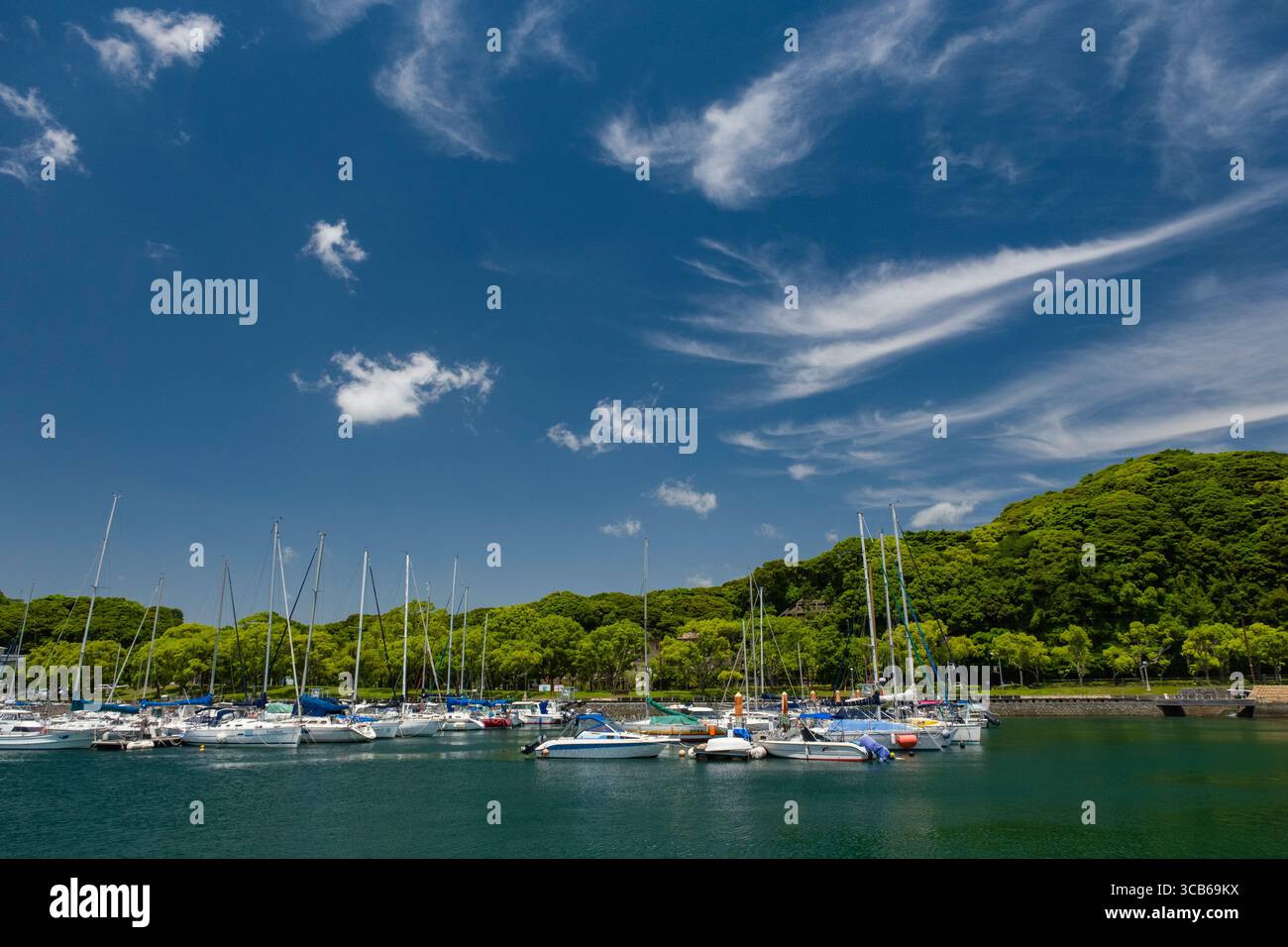 Un pittoresco porticciolo con yacht attraccati sotto un cielo blu luminoso con lussureggianti colline verdi. La scena serena cattura la tranquillità di una giornata perfetta Foto Stock