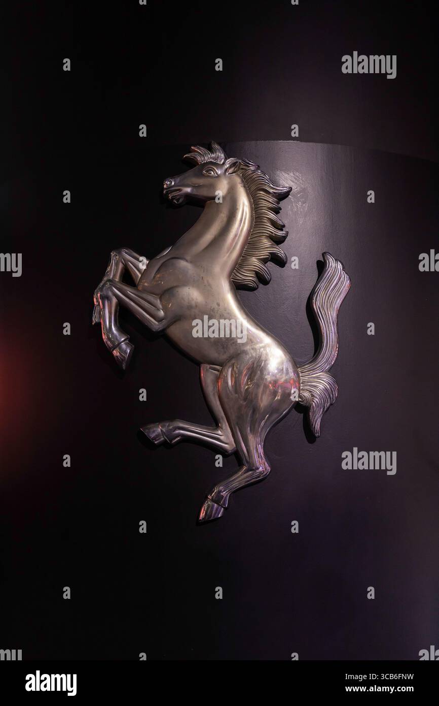 Emblema di cavallino in cromo lucido su una parete nera presso il Museo Ferrari di Maranello, in Italia, simbolo iconico del patrimonio delle corse Foto Stock