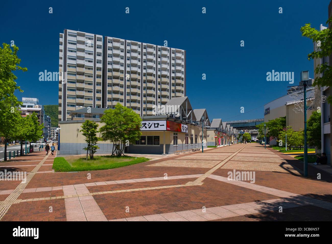 Il quartiere urbano presenta un moderno e alto appartamento, una passerella pavimentata ben tenuta, vegetazione e un'area commerciale sotto un cielo azzurro, con Foto Stock