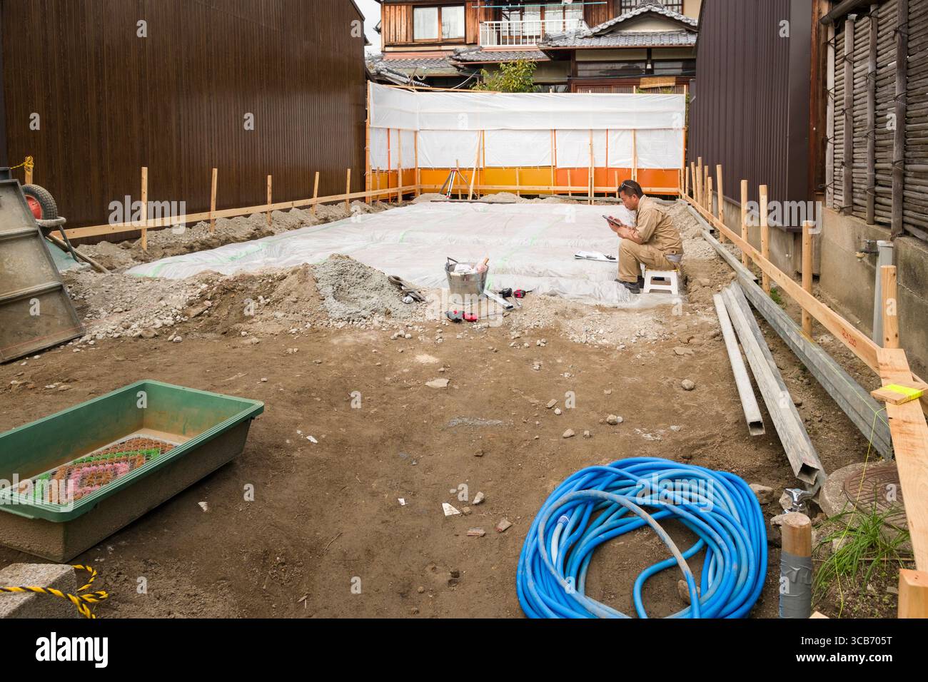 Un operaio edile che si riposa brevemente in un cantiere, circondato da strumenti, materiali e preparazione del terreno per una nuova struttura, Kyoto, Giappone Foto Stock