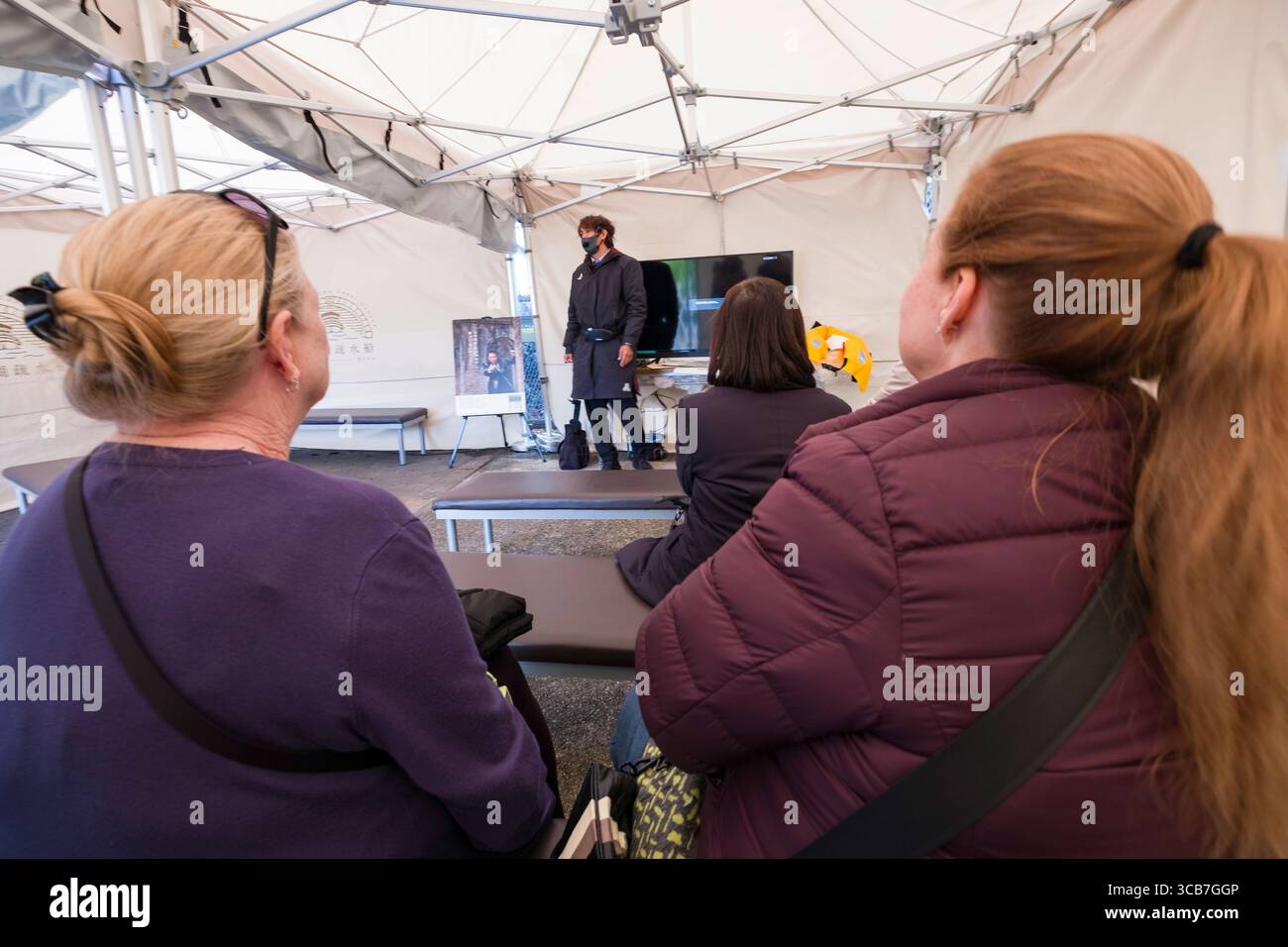 Un piccolo gruppo di persone che partecipano a una presentazione all'interno di una tenda esterna coperta prima dell'inizio della crociera sul canale del lago Biwa, Kyoto Foto Stock