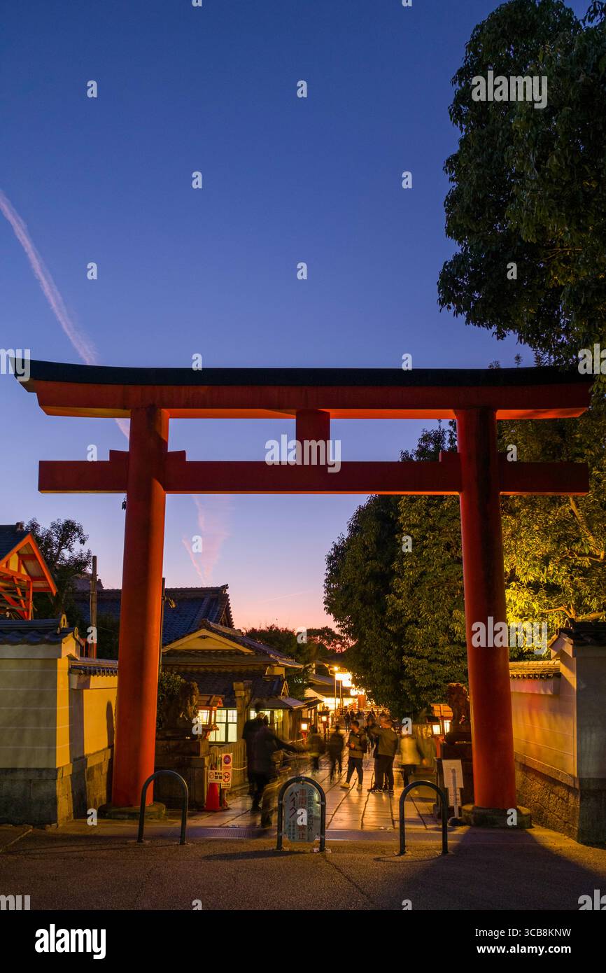 Una pittoresca porta torii rossa conduce al Santuario di Yasaka illuminato al crepuscolo, abbracciando la tradizione e la cultura giapponesi in un ambiente sereno. Foto Stock