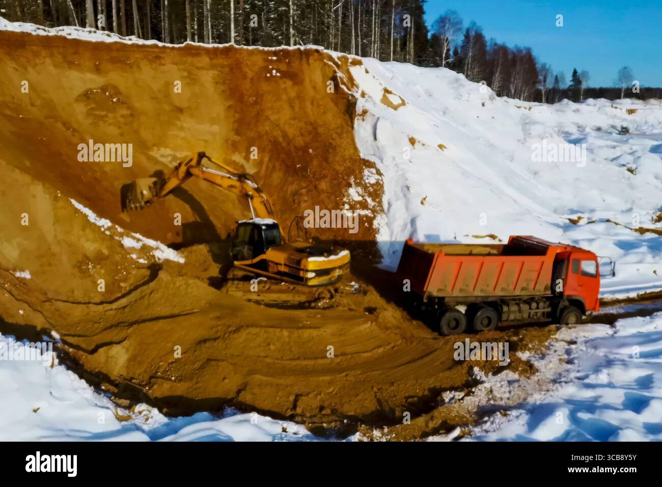 Un dumper arancione in inverno in una cava di sabbia innevata. Foto Stock