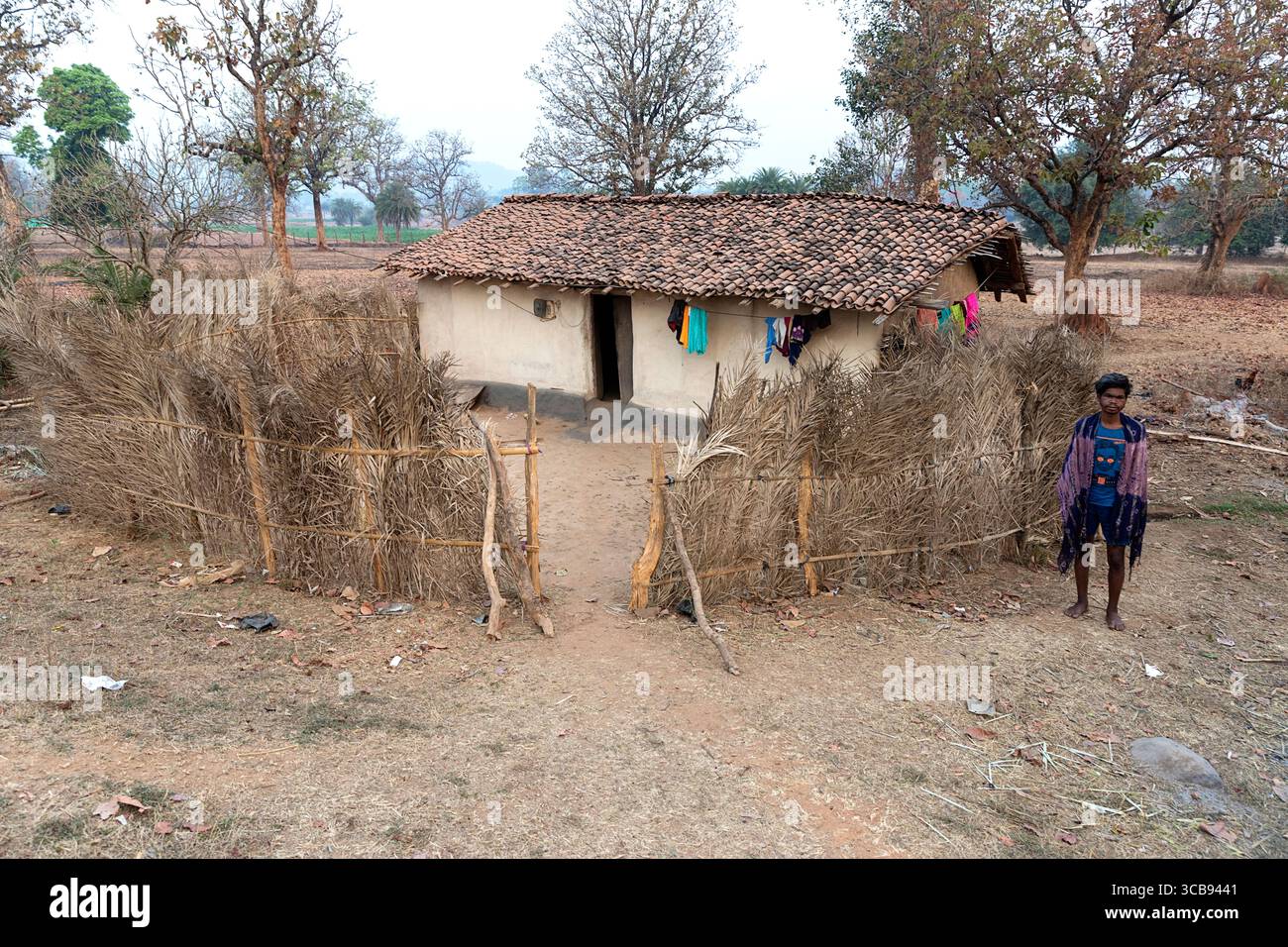 Uomo locale in piedi di fronte alla sua casa tradizionale fatta a mano fatta di fango, recinzione fatta con rami a Chhattisgarh in india Foto Stock