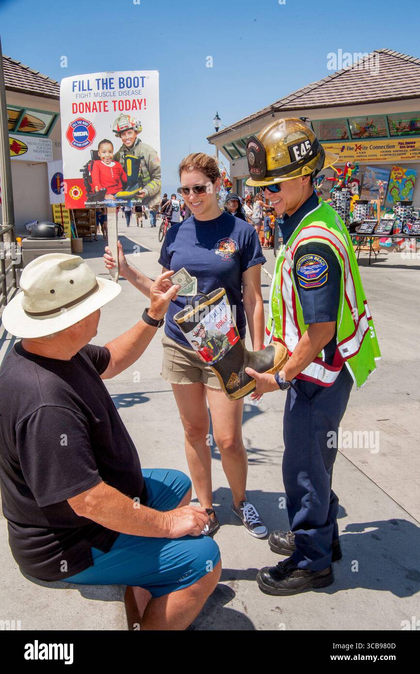 9 luglio 2016: Un vacanziere a Huntington Beach Pier, California, mette una donazione di beneficenza per aiutare a combattere le malattie muscolari in uno stivale tenuto da un vigile del fuoco. (Immagine di credito: © Spencer Grant/ZUMA Press Wire) Foto Stock