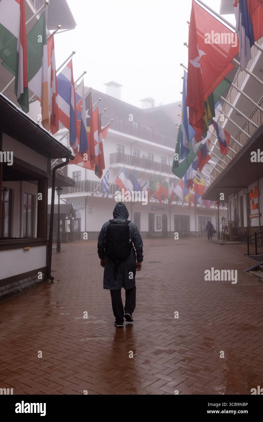 SOCHI, RUSSIA - 3 MAGGIO 2024: Un uomo cammina attraverso il villaggio olimpico, il villaggio olimpico con vista sugli edifici e le bandiere nazionali di diversi paesi Foto Stock