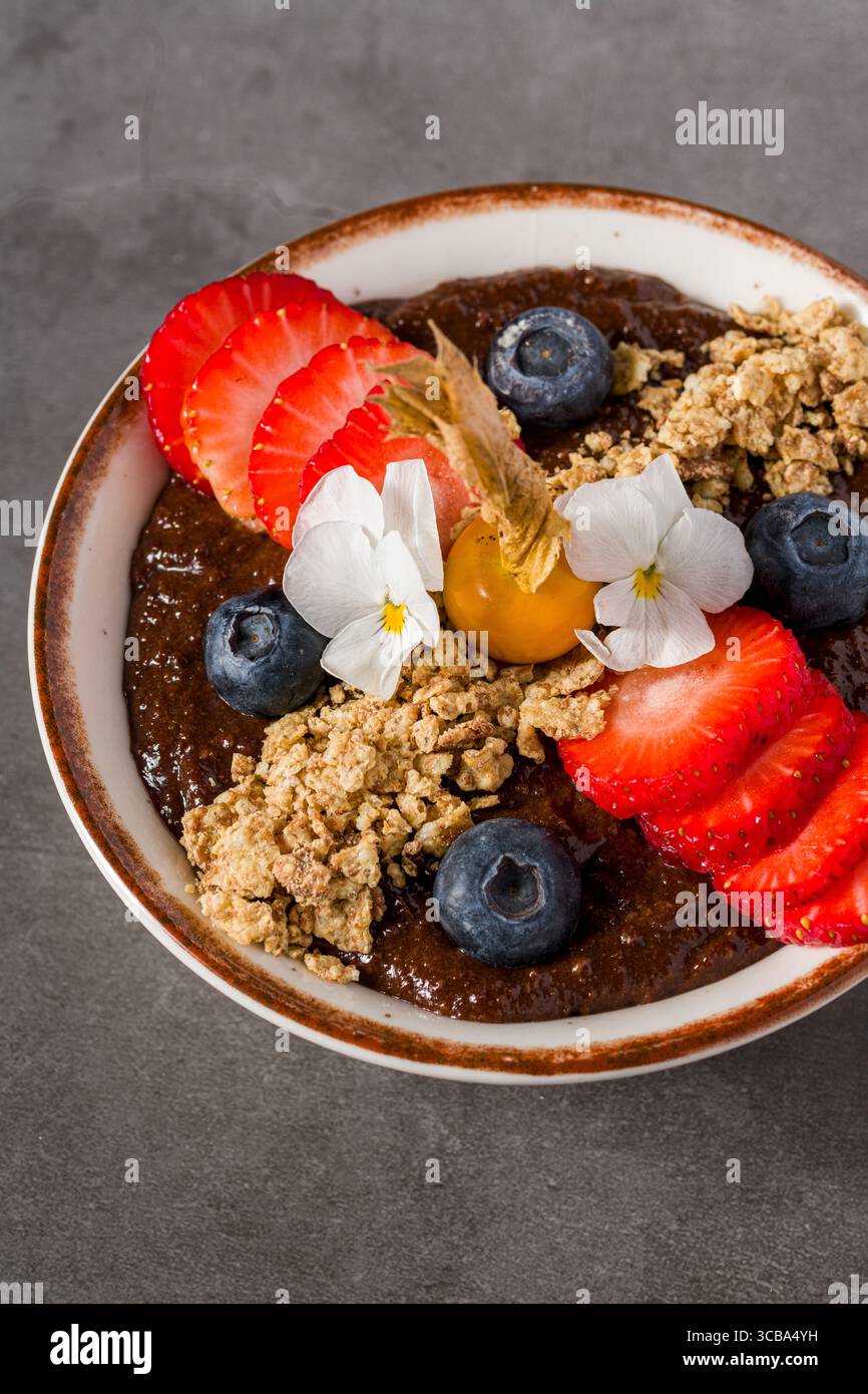 Ciotola per frullati di cioccolato tropicale con muesli, frutti di bosco e fiori commestibili Foto Stock