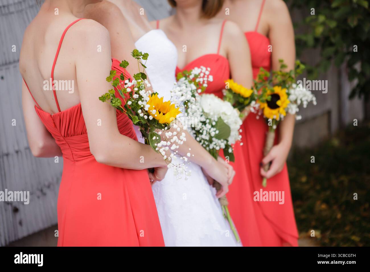 Le damigelle rivestite di corallo circondano la sposa che tiene mazzi di girasole Foto Stock